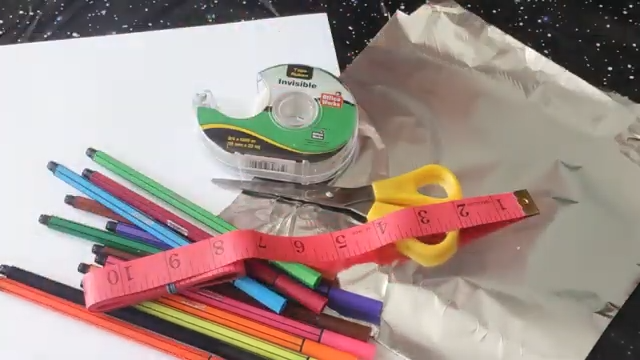 A pile of craft supplies including paper, aluminum foil, a pair of scissors, ruler and a roll of tape.