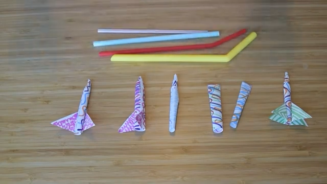 Small paper rockets and a handful of straws on a wooden tabletop.